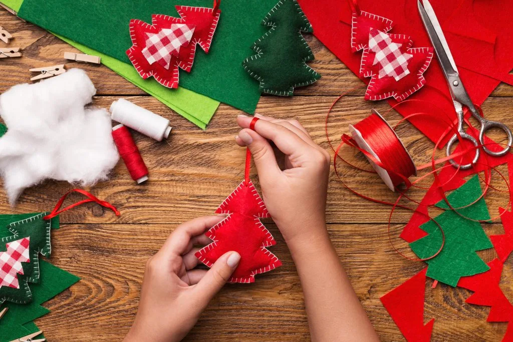 Woman made Christmas tree decoration of felt. Hands holding Xmas tree ornament, sitting at workplace, top view