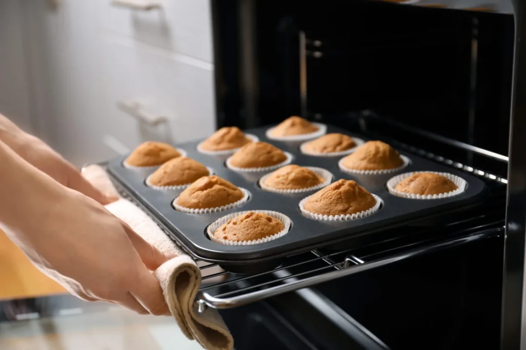 Woman taking baking tray with cupcakes from oven