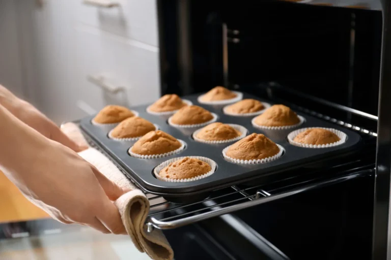 Woman taking baking tray with cupcakes from oven