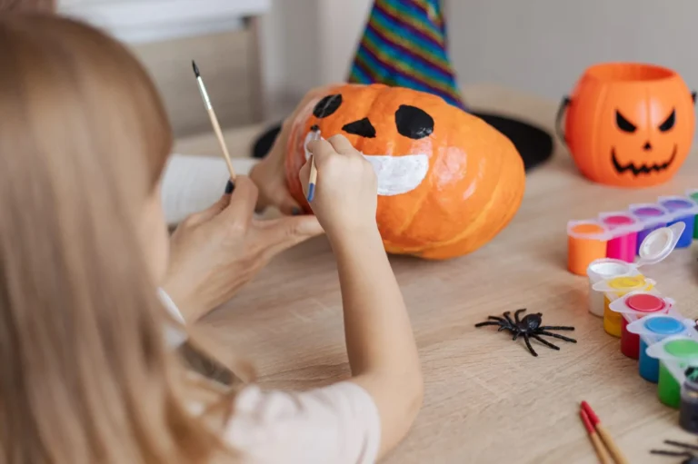 child with mother painting Halloween pumpkins together at home, happy family mother and kid preparing handmade decorations for Saints Day party